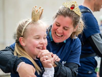 Kvinde og barn i Royal Run-trøjer griner sammen og har små kroner på.