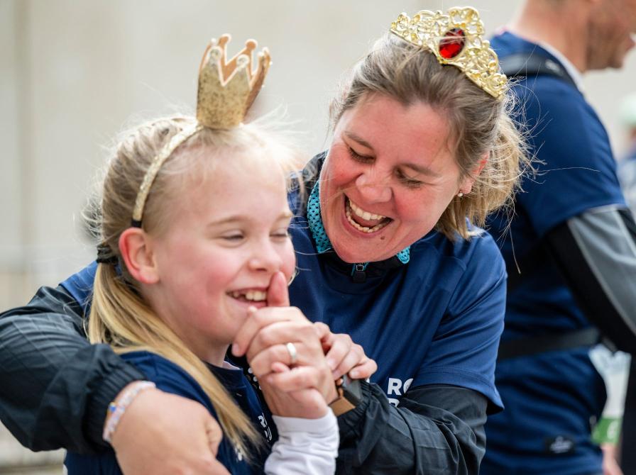 Kvinde og barn i Royal Run-trøjer griner sammen og har små kroner på.